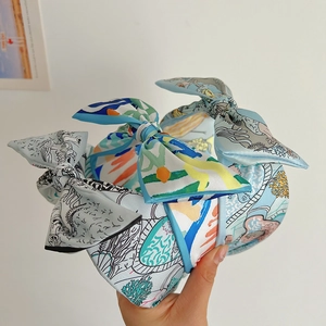 Detail of light blue silk bow headband with nautical prints held by a hand