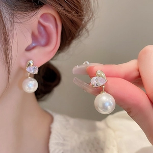 Close-up of elegant gold heart earrings with sparkling crystals and white round pearls
