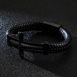 Macro detail of men's black braided leather bracelet featuring a metal cross charm