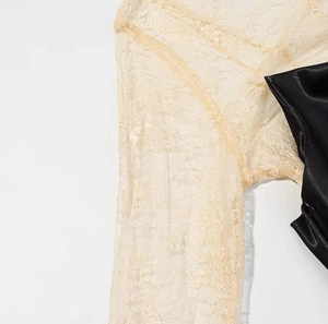 Détail de la manche en dentelle beige et du tissu en satin noir sur une robe nuisette
