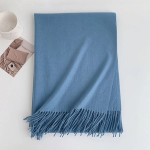Detail of blue faux cashmere scarf with tassels styled with coffee and magazine