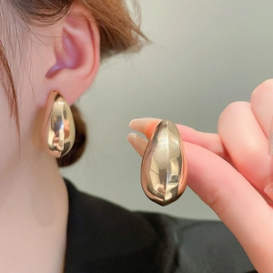 Close-up of model wearing large golden teardrop earrings with a smooth metallic finish
