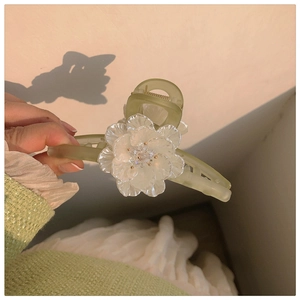 Macro detail of a green hair claw clip with a delicate white resin flower and bead center