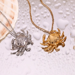 Primer plano de collares con colgante de cangrejo en oro y plata sobre espejo de agua