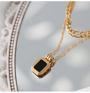 Detailed close-up of double-layer gold necklace featuring a black rectangular pendant