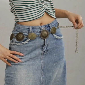 Détail d'une chaîne de taille en métal bronze vintage avec disques sur jupe en jean