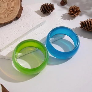 Detail of wide resin bangles in green and blue colors on a natural stone base