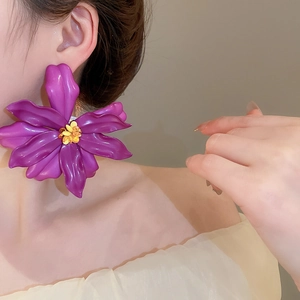 Close-up of oversized purple acrylic flower earrings worn by a model for a beach holiday style