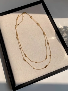 Detail of double-layer golden bead necklace with lobster clasp on beige textured background
