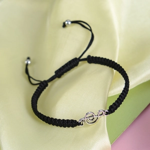 Macro view of adjustable black braided rope bracelet with silver treble clef music charm