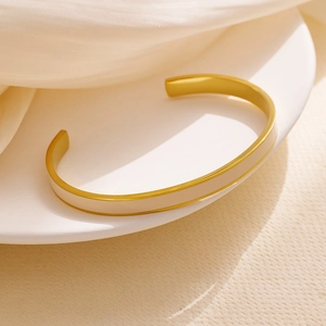 Detail eines minimalistischen goldenen C-Armreifs mit eleganter cremefarbener Emaille
