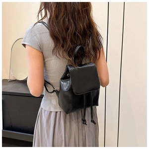 Close-up of black leather mini backpack featuring drawstring closure and flap cover