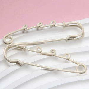 Detail of 6cm beige painted safety pins with three loops on a pink and white grid base
