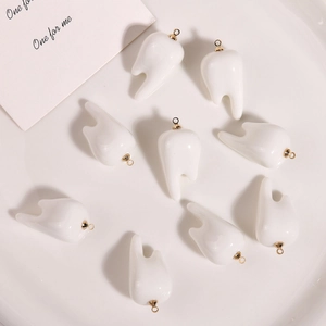 Flat lay of nine 3D resin tooth pendants with gold loops for DIY jewelry making
