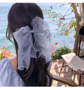 Close-up of a large light blue organza bow hair clip worn by a model against a seaside view