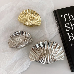 Glossy shell-shaped hair claw clips in gold and silver finish on artistic white background