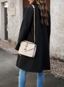 Detail of beige crossbody bag with metal chain strap shown on model against a street wall