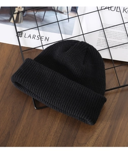 Flat lay of a classic black knitted beanie hat on a wooden desk with Nordic style decor