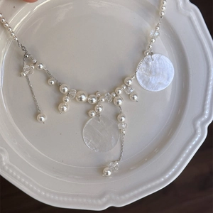 Detail of beaded tassel necklace with white pearls and round shell pendants on ceramic tray