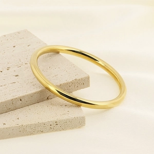 Classic 6mm polished gold stainless steel bangle displayed on travertine stone