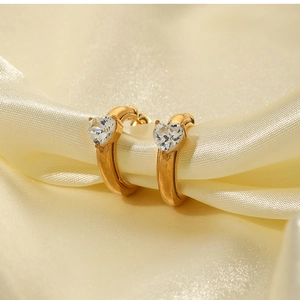 Macro shot of gold-plated C-shaped heart zircon earrings on luxurious silk fabric background