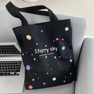 Détail du sac cabas en toile noire avec imprimé Starry Sky posé sur un canapé en tissu