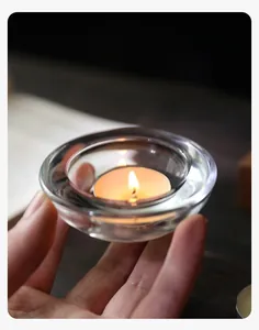 Nahaufnahme vom Teelichthalter aus Kristallglas mit brennender Kerze in der Hand