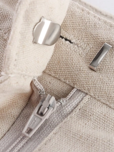 Close-up of linen shorts waist featuring silver metal hook and bar closure with zipper