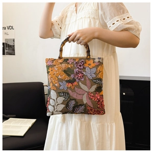 Detailed view of linen handbag with floral embroidery, sequins, and bamboo handle.