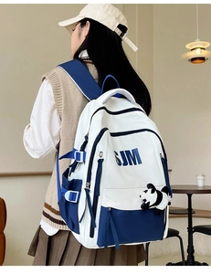 Detail of white and navy blue canvas backpack with panda charm on model in cafe