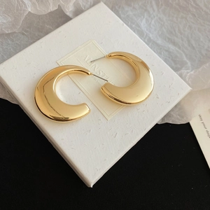 Macro shot of chunky gold C-shaped hoop earrings with a mirror-finish on a display card