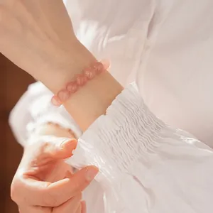 Bracelet élégant en perles de quartz fraise naturel porté au poignet avec manche blanche