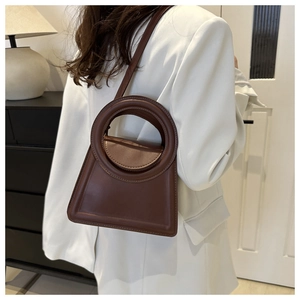 Close-up of a brown trapezoid leather handbag with a round handle on a white suit model