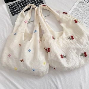 Detail of embroidered cherry and butterfly patterns on cream-colored tote bags