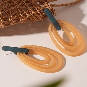 Detail of layered geometric oval resin earrings in navy and amber on woven background