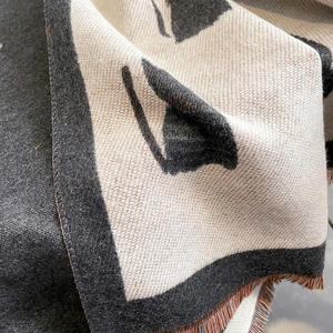 Detail shot of black and beige cat pattern scarf with orange tassels and woven texture