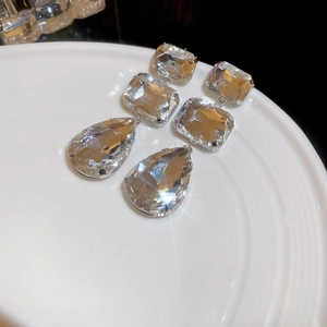 Detailed view of silver drop earrings with geometric crystals on a white ceramic tray