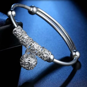 Silver-plated bangle with engraved floral cylinders and hollow bell charm on a dark surface
