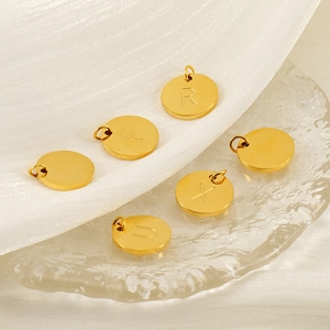 Macro detail of gold round alphabet pendants R F X U on textured glass and white fabric