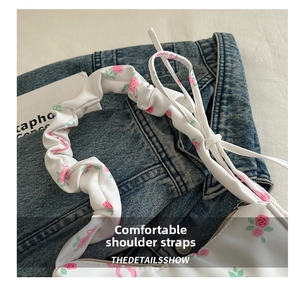 Close-up of the ruffled wide shoulder strap with floral patterns and drawstring details