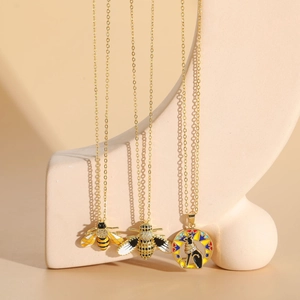 Detailed shot of 14K gold plated bee and Egyptian cat pendants with enamel and zircon