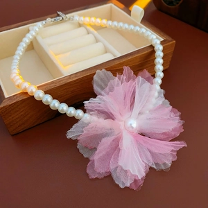 Detail shot of pearl necklace with pink tulle flower pendant in a wooden jewelry box
