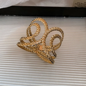 Detailed view of wide gold-toned twisted rope cuff bracelet on white textured surface