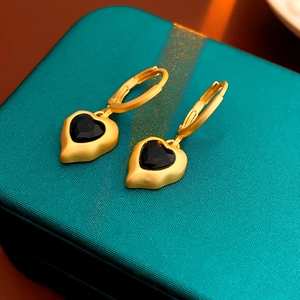 Dettaglio di orecchini vintage dorati con cuore nero su scatola verde strutturata