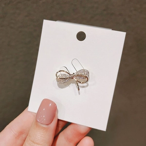 Detail of a sparkling golden bow brooch with white crystals on a white display card
