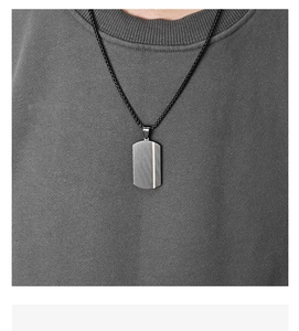 Detail of black military dog tag pendant with vertical texture and gold stripe on woven chain