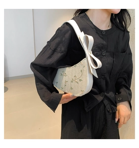 Detail of straw woven shoulder bag with floral embroidery and large ribbon bow on strap
