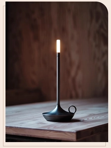 Detail of modern black metal candle-style LED lamp on wooden table with warm light