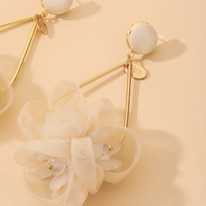 Macro detail of beige fabric flower earring with crystal center and golden metal frame