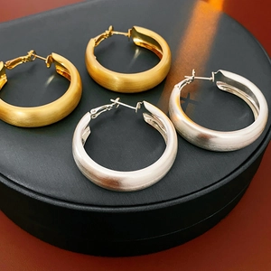 Dettaglio di orecchini a cerchio in oro e argento con texture metallica spazzolata